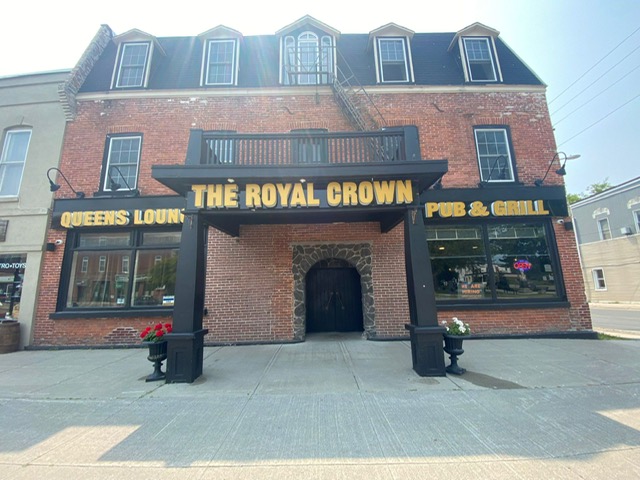 Red-brick Royal Crown facade with gold pub signage, a black entrance canopy and an arched stone doorway