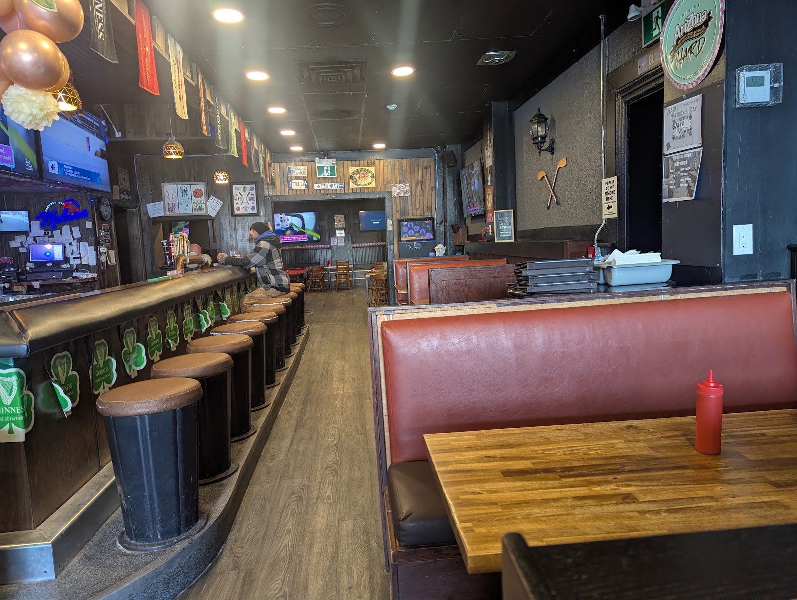 Pub interior with a long bar, padded stools, red-brown booths, wooden tables and televisions